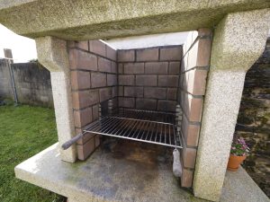 Detalle de la gran parrilla de obra con leña preparada en el exterior de Casa Bieiteiros, lista para cocinar en Valdoviño
