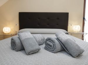 Primer plano de toallas de cortesía enrolladas sobre la cama con un elegante cabecero oscuro de fondo en Casa Bieiteiros
