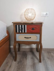 Primer plano de una mesita de noche de madera con una lámpara encendida, una planta decorativa y un libro en un dormitorio de Casa Bieiteiros, Valdoviño