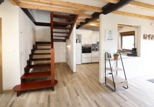 Vista de la zona de entrada en Casa Bieiteiros, mostrando las escaleras de madera a la izquierda y el acceso a la cocina moderna a la derecha