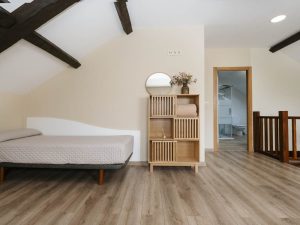 Vista de una cama individual en la buhardilla de Casa Bieiteiros con acceso a un baño al fondo y techo de madera abuhardillado en Valdoviño