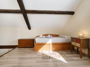 Vista de la cama situada en el lateral izquierdo de la buhardilla de Casa Bieiteiros, con techos de madera y ambiente luminoso en Valdoviño