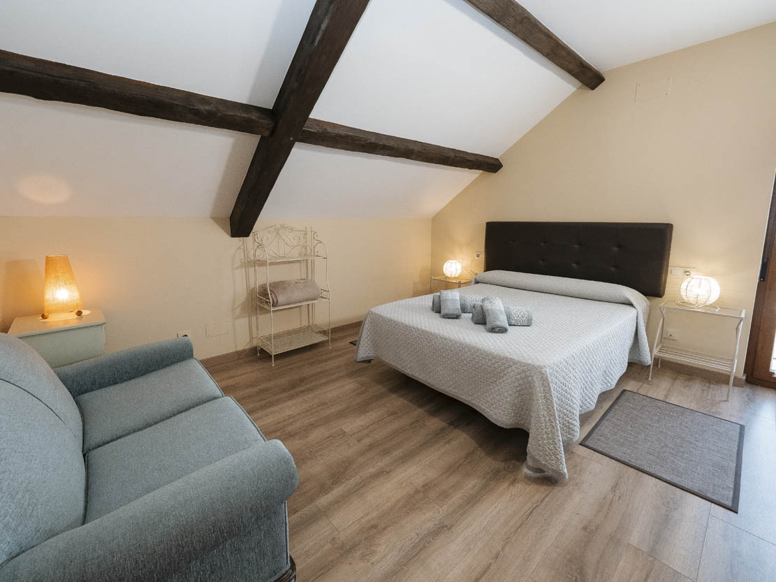 Vista de una habitación con dos camas y un sofá de color oscuro a la izquierda, en la planta alta de Casa Bieiteiros, Valdoviño