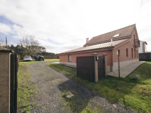 Vista de la entrada principal a la finca de Casa Bieiteiros en Valdoviño, con el portalón metálico abierto, mostrando el acceso al jardín y la casa a la derecha