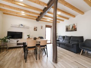 Amplio salón comedor de Casa Bieiteiros con gran sofá gris, mesa de madera y techo de vigas vistas, perfecto para grupos en Valdoviño